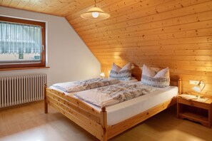 Un lit en bois avec une tête de lit, une table de chevet avec une lampe, une fenêtre avec des rideaux et un radiateur.
