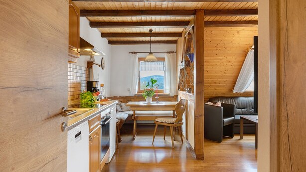 A kitchen with wooden cabinets, a dining table with chairs, a sofa, and a window with a view. - Apartment 'Ferienwohnung Abendrot' with Mountain View, Shared Garden and Wi-Fi (Breitnau)