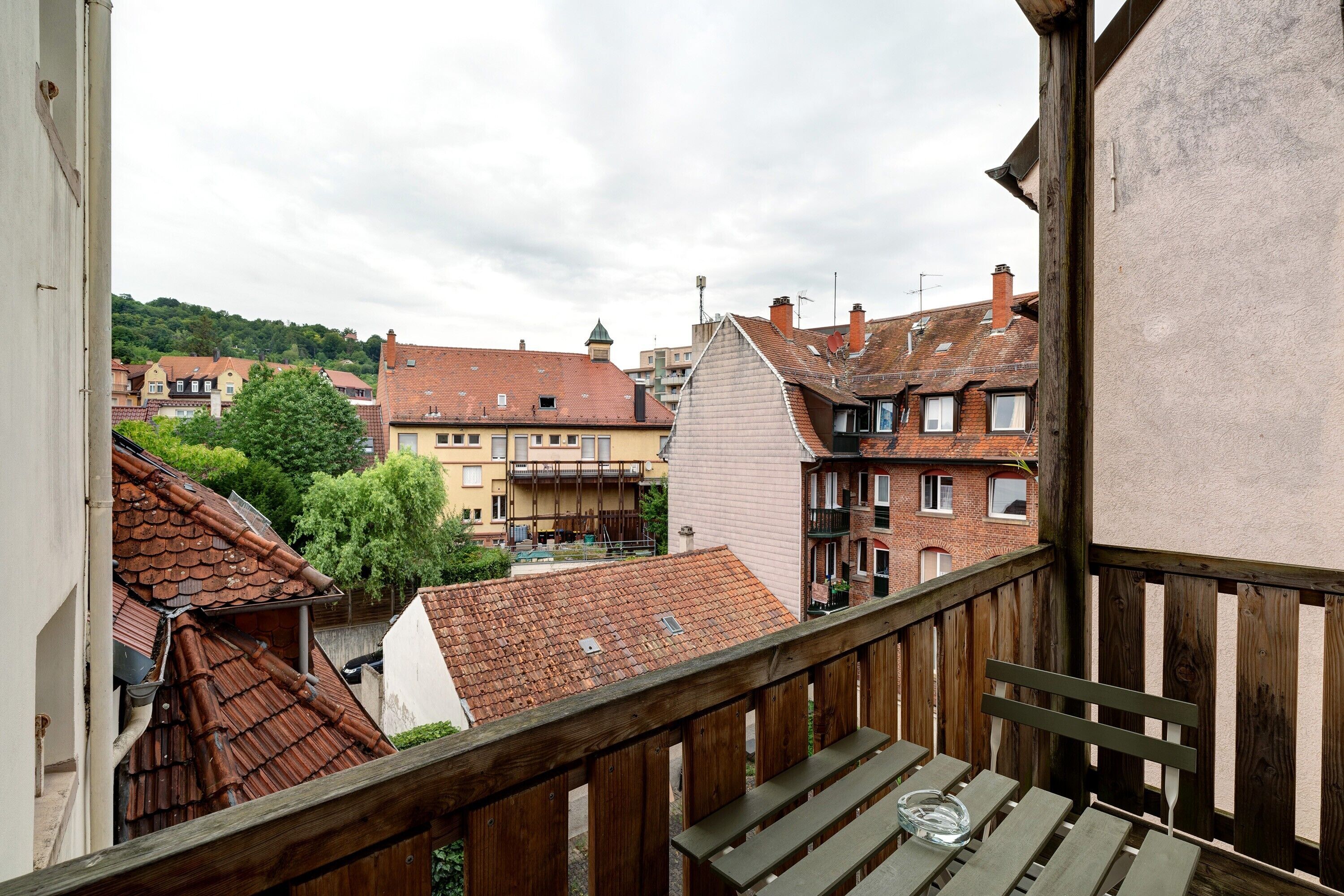Un balcon doté de balustrades en bois, donnant sur un quartier résidentiel avec différents immeubles et un arbre.