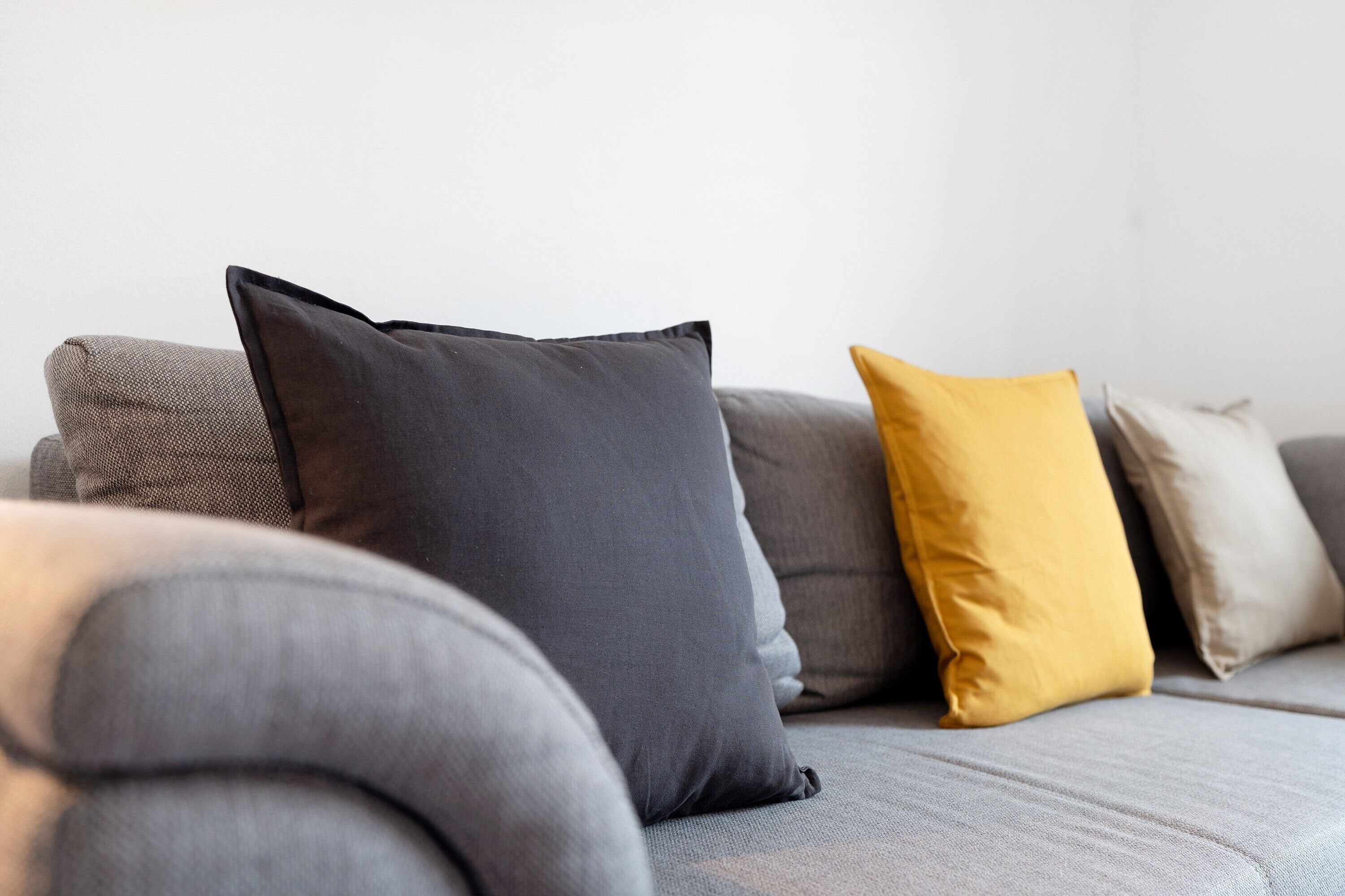 A grey sofa with three cushions in different colors.