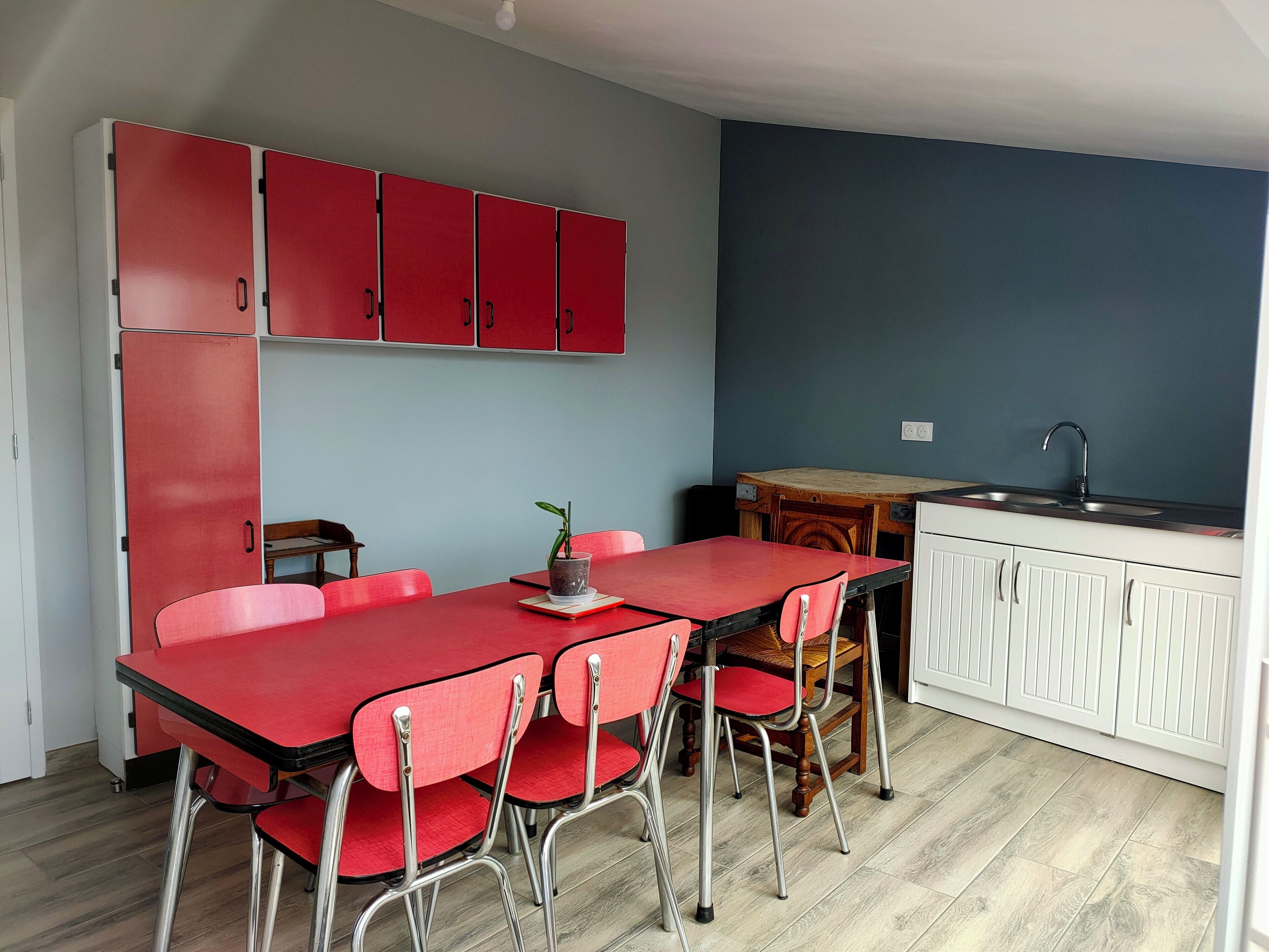 A compact kitchen with red cabinets, a wooden dining table with red chairs, and a small sink.