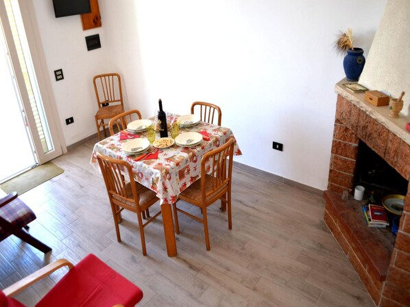 Un coin repas avec une table dressée pour quatre personnes, entouré de chaises en bois, d’une cheminée et d’un téléviseur fixé au mur.
