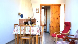Uma sala de jantar com uma mesa posta para quatro pessoas, uma poltrona vermelha e uma porta de madeira que dá para outro cômodo.