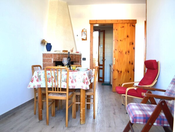 A dining area with a table set for four, a red lounge chair, and a wooden door leading to another room.