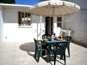 Une terrasse extérieure avec une table, des chaises, un parasol et un espace cuisine.