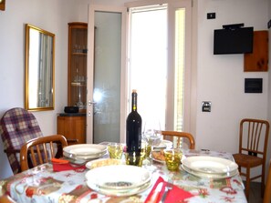 Un coin repas avec une table dressée pour quatre personnes, une bouteille de vin et un téléviseur fixé au mur.