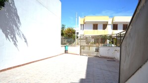 Um pátio com piso de azulejos, um portão de metal e uma parede branca.