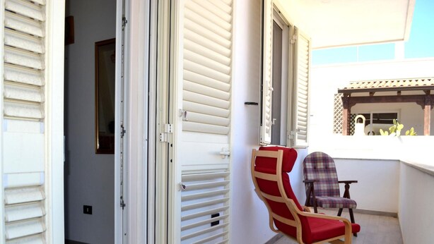 Uma varanda com uma cadeira de madeira, uma cadeira xadrez e uma porta branca.