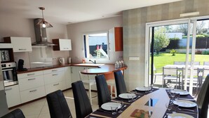 A modern kitchen with white cabinets, a stainless steel range hood, and a large window overlooking a garden. - Gîte Avec Très Belle vue mer SPA Jacuzzi à Sables D'or les Pins 400m de la Plage (Plurien)