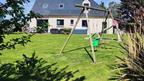 A house with a sloped roof, a front porch, and a small garden area with a swing set. - Gîte Avec Très Belle vue mer SPA Jacuzzi à Sables D'or les Pins 400m de la Plage (Plurien)