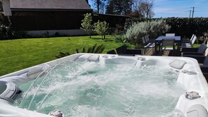 A hot tub with water jets, surrounded by a patio area with chairs and a table. - Gîte Avec Très Belle vue mer SPA Jacuzzi à Sables D'or les Pins 400m de la Plage (Plurien)
