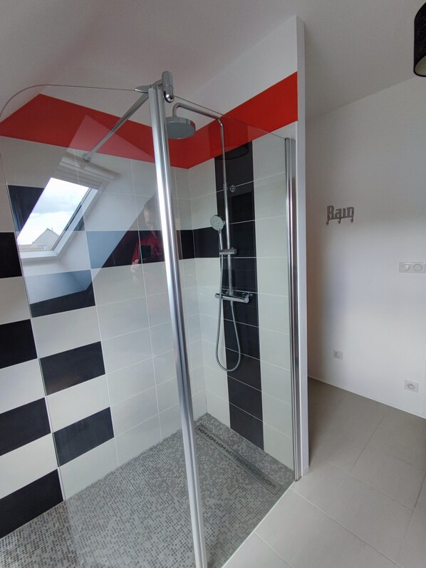 A modern bathroom with a glass shower enclosure, a skylight, and a checkered floor pattern.