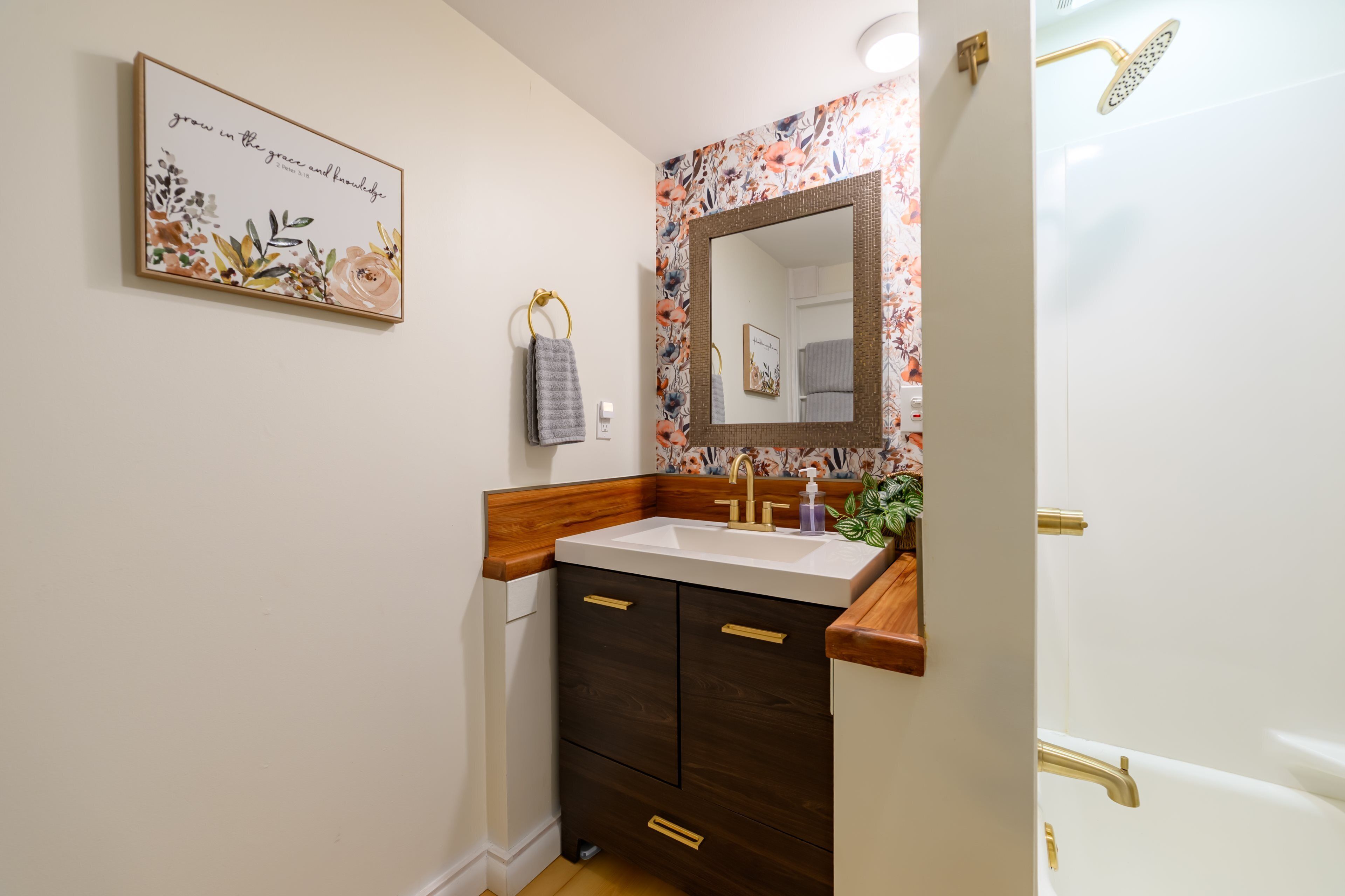 Une salle de bain avec un meuble-lavabo en bois, un grand miroir et une douche dotée d’un robinet doré.