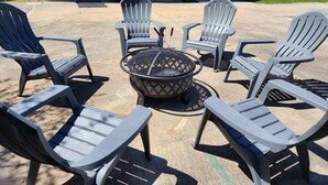 Une terrasse avec des fauteuils Adirondack disposés autour d’un foyer, une maison en arrière-plan et un ciel dégagé.