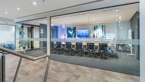 Een moderne kantoorruimte met glazen scheidingswanden, meerdere werkplekken en een groot digitaal scherm.
