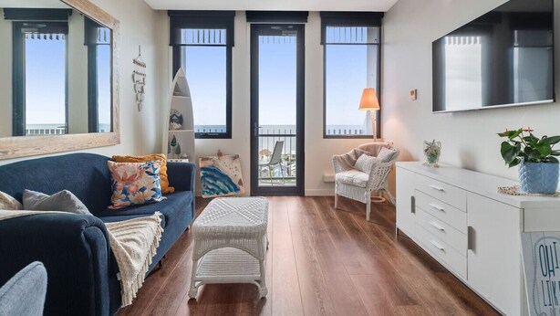 Een moderne woonkamer met een blauwe bank, een witte rieten poef en een wit kastje.