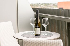 A bottle of Riesling wine on a table with two glasses, a white chair, and a balcony railing.