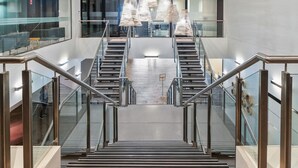 Een modern interieur met een centrale trap, begrensd door glazen leuningen, die naar een lager gelegen niveau leidt.