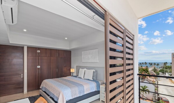 A bedroom with a bed, wardrobe, and a view of a coastal area.