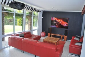 Un salon moderne avec des canapés en cuir rouge, une table basse en bois, un grand téléviseur et un ballon d’exercice rouge.