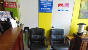 Un área de recepción con dos sillones de cuero negro, un mostrador de madera y un cartel que indica que se requiere identificación con foto para el registro.