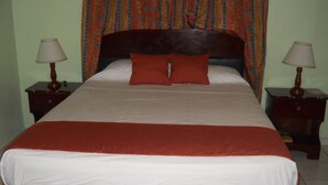 Una cama con cabecera de madera, dos mesitas de noche con lámparas y una cortina estampada.