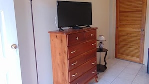 Un aparador de madera con un televisor encima, una lámpara sobre una mesita auxiliar y una puerta de madera al fondo.