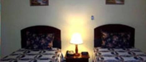 Une chambre avec deux lits, une table de chevet avec une lampe et deux tableaux accrochés au mur.