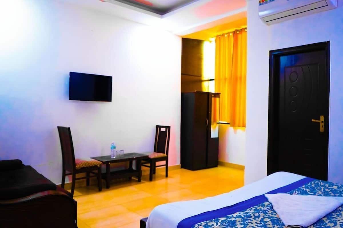 Ein Hotelzimmer mit einem Bett, einem Schreibtisch mit Stühlen, einem an der Wand befestigten Fernseher und einer Klimaanlage.