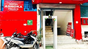 The entrance to Ashoka Palace Hotel with a red facade, a visible assembly station sign, and a staircase leading inside. - Airport Hotel Ashoka Palace (New Delhi)