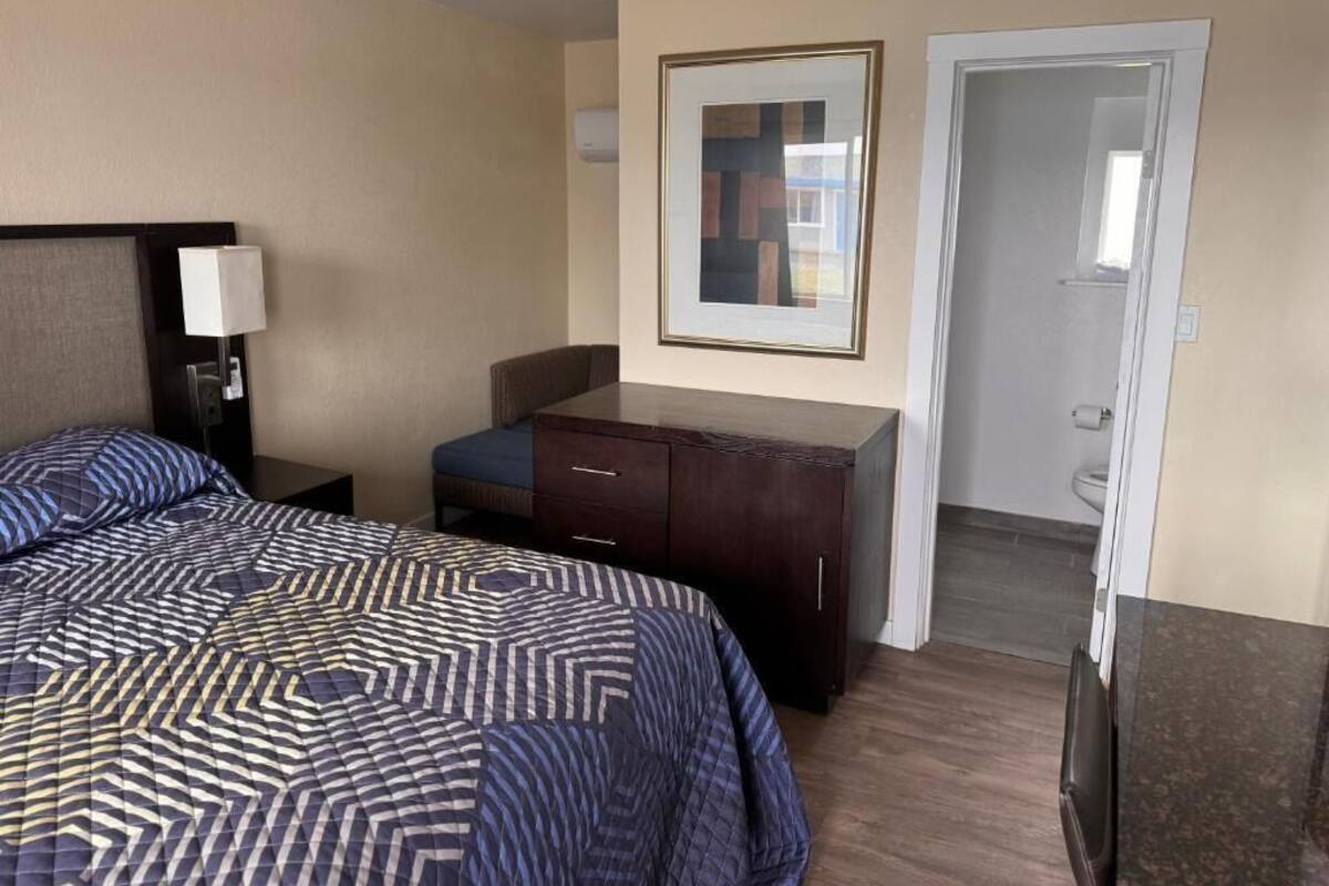 A hotel room with a large bed, a dresser, a chair, and a door leading to the bathroom.