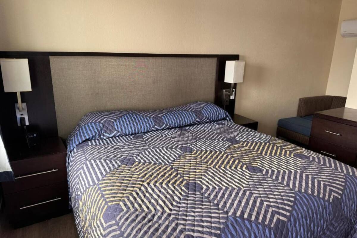 A hotel room with a large bed, two bedside tables, a nightstand, and a dresser.