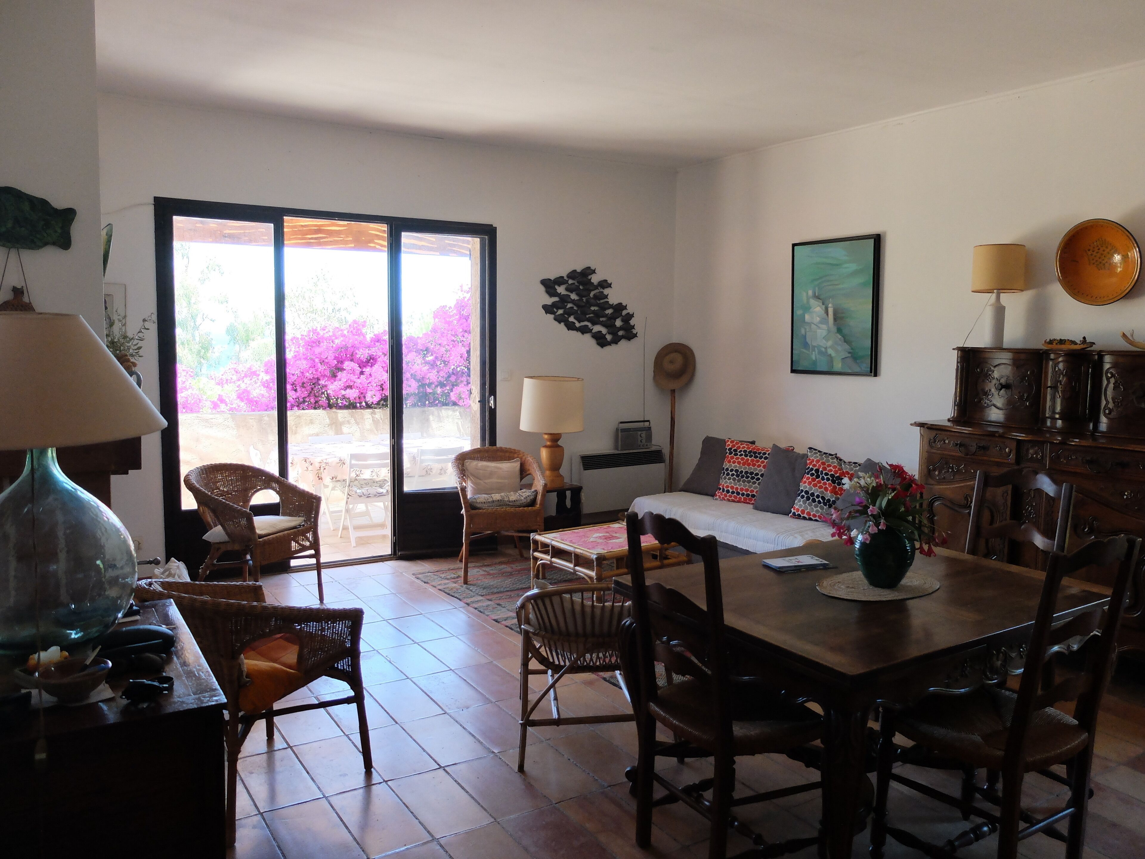 Un vaste espace de vie comprenant une table à manger, des chaises, un canapé et une grande fenêtre donnant sur des fleurs roses.