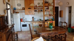 A traditional kitchen with wooden cabinets, a dining table, and chairs. There is a refrigerator, oven, and various kitchen utensils. - Loue Maison de Famille Dans le Golf de Lava à Proximité de la mer (Villanova)