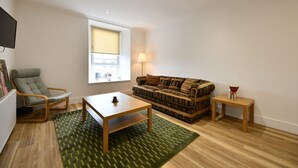 A living room with a sofa, a chair, a coffee table, a lamp, and a small table with a vase. - Troon Portland Apt A (Troon)