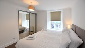 A modern hotel room with a large bed, a sliding door closet, a window with a view, and a ceiling light. - Troon Portland Apt A (Troon)
