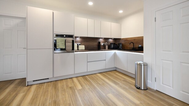 A modern kitchen with white cabinetry, a stainless steel trash can, and a wooden floor. - Troon Portland Apt A (Troon)