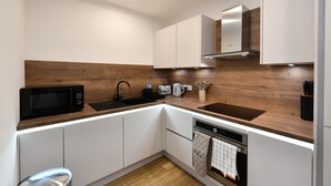 A modern kitchen with white cabinets, a wooden countertop, a black microwave, a sink, and a stainless steel range hood. - Troon Portland Apt B (Troon)