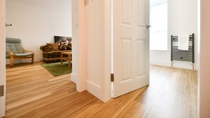 A room with wooden flooring, a green rug, a wooden chair, a sofa, and a painting on the wall. - Troon Portland Apt B (Troon)