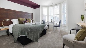 Ein Schlafzimmer mit Bett, Nachttisch, Lampe und Schreibtisch mit Stühlen.