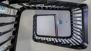 Eine Ecke eines Raumes mit einer weißen Wand, einem schwarzen Metallgeländer und einem kleinen runden Gegenstand an der Wand.