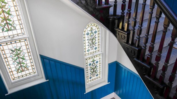 Eine Treppe mit blauen und weißen Wänden, Holzspindeln und Glasfenstern mit Buntglas.