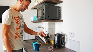 Eine Person gießt ein Getränk in eine Tasse auf einer Küchenarbeitsplatte mit einer Mikrowelle und einer Kaffeemaschine.