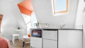 A compact kitchen with white cabinetry, a built-in oven, and a sink. There is a small white stool and a plant on the counter. - Eco Aparthotel - Heights Studio (Folkestone)