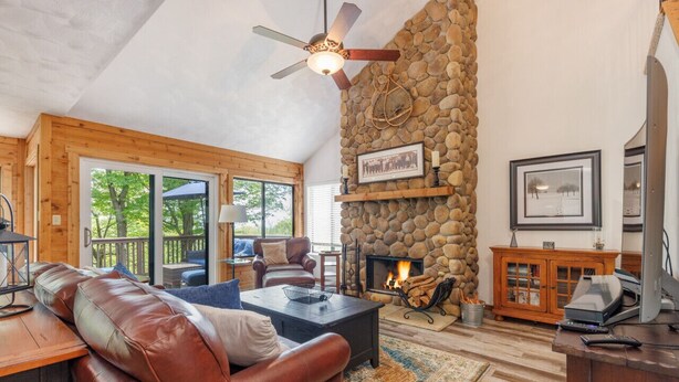 A cozy living room with a stone fireplace, leather sofa, and a ceiling fan. - HV Woodside, Baby Grand Piano (Hidden Valley)