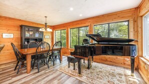 A wooden cabin interior with a dining area, a piano, and large windows. - HV Woodside, Baby Grand Piano (Hidden Valley)