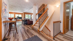 A spacious living area with a wooden staircase, a dining table with chairs, and a cozy seating area. - HV Woodside, Baby Grand Piano (Hidden Valley)