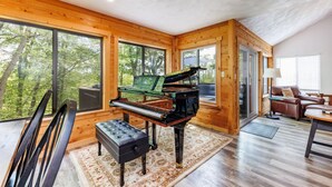 A wooden interior with a grand piano, large windows, and a cozy seating area. - HV Woodside, Baby Grand Piano (Hidden Valley)