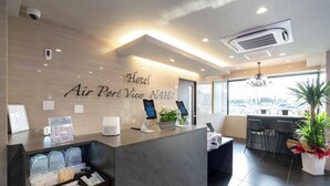 Un espace d’accueil d’hôtel au design moderne, comprenant un comptoir d’accueil, une grande fenêtre offrant une vue et une plante dans un coin.