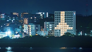 Une vue nocturne d’une ville, avec des bâtiments illuminés le long d’une promenade au bord de l’eau.